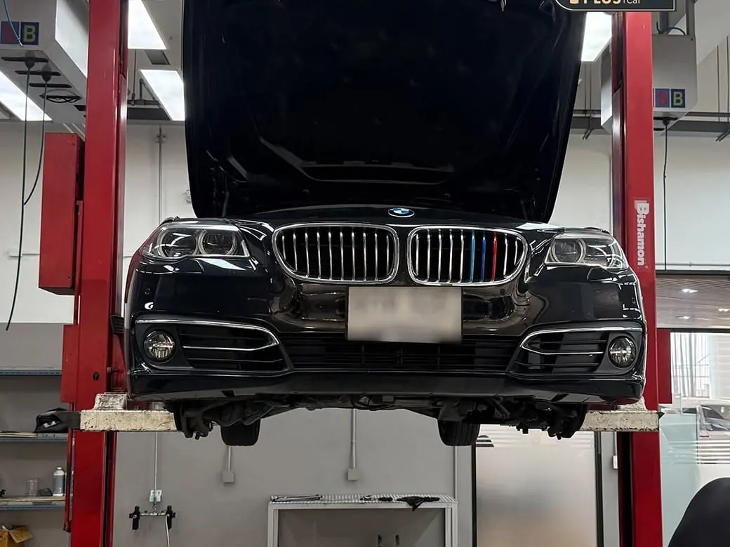 รถ BMW ซีรีส์ 5 ถูกยกขึ้นบนลิฟต์สองเสาในอู่ P-Plus BM Service เปิดฝากระโปรงพร้อมตรวจจากใต้ท้องรถ